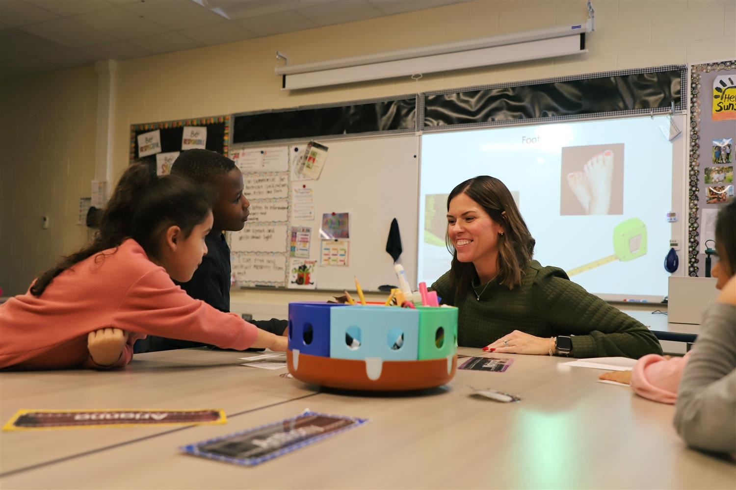 Mrs. Splatts smiling with students at their desk during class.